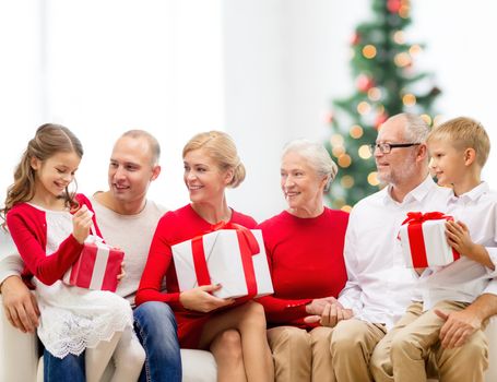 family, holidays, generation and people concept - smiling family with gift boxes sitting on couch over living room with christmas tree background