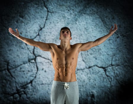 sport, bodybuilding, strength and people concept - young man standing with raised hands over concrete wall background