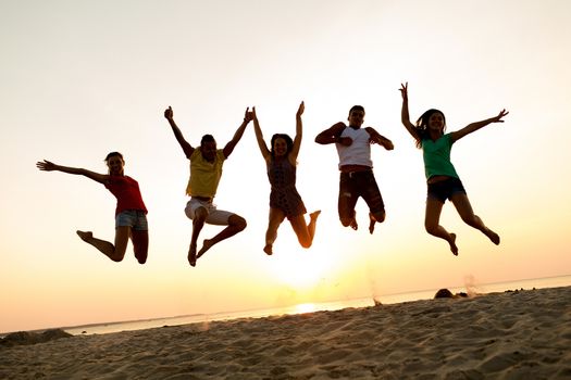 friendship, summer vacation, holidays, party and people concept - group of smiling friends dancing and jumping on beach