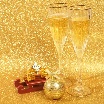 Two glasses of champagne with golden glitter lights on background