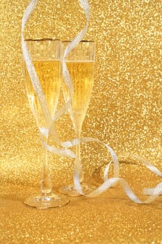 Two glasses of champagne with golden glitter lights on background