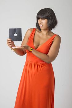 Philipino woman wearing a low cut orange dress pointing at a five inch floppy drive looking disturb