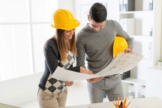 Smiling architect looking the architectural plans in office.