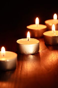 Set of lighting candles on wooden board against dark background