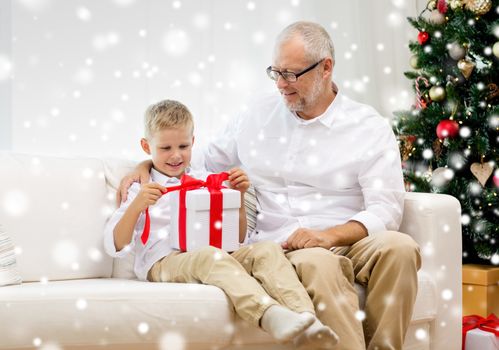 family, holidays, generation, christmas and people concept - smiling grandfather and grandson with gift box sitting on couch at home