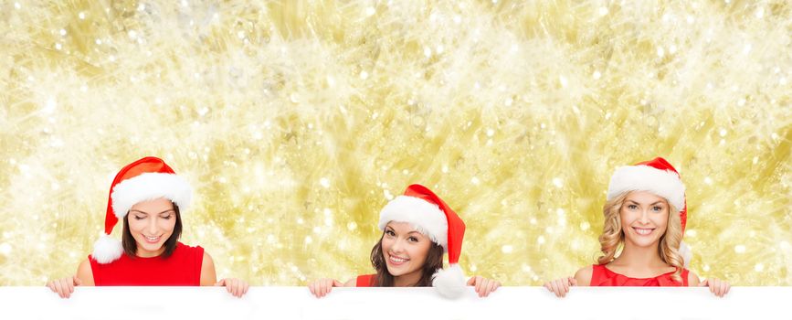 christmas, x-mas, people, advertisement and sale concept - happy women in santa helper hat with blank white board over yellow lights background