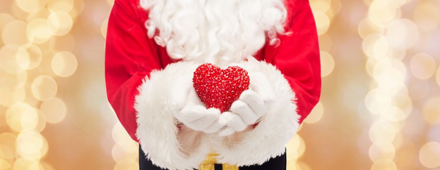 christmas, holidays, love, charity and people concept - close up of santa claus with heart shape decoration over beige lights background