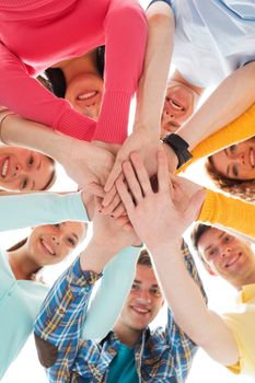 friendship, youth and people concept - group of smiling teenagers with hands on top of each other