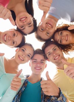 friendship, youth, gesture and people - group of smiling teenagers in a circle showing thumbs up