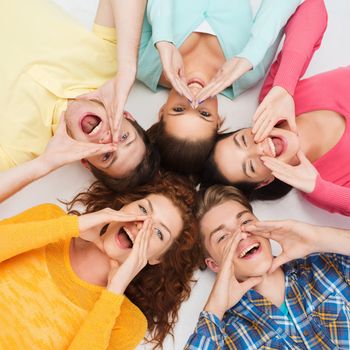 friendship, youth, gesture and people - group of smiling teenagers lying on floor in circle and shouting