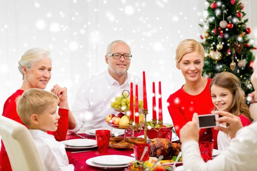 family, holidays, generation, christmas and people concept - smiling family having dinner and making photo with camera at home