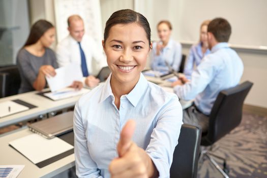 business, people, gesture and teamwork concept - smiling businesswoman showing thumbs up with group of businesspeople meeting in office