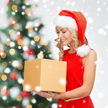 holidays, celebration and people concept - smiling woman in santa helper hat and red dress with gift box over christmas tree lights background