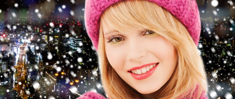 happiness, winter holidays, christmas and people concept - close up of smiling young woman in pink hat and scarf over snowy night city background