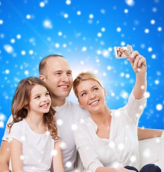 family, holidays, christmas, technology and people - smiling family making selfie with camera over blue snowy background