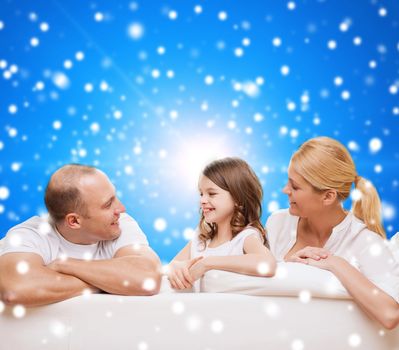 family, childhood, holidays and people - smiling mother, father and little girl over blue snowy background