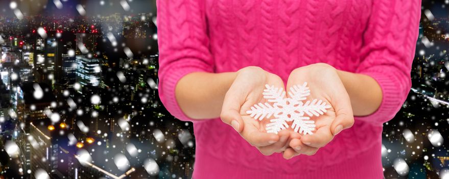christmas, holidays and people concept - close up of woman in pink sweater holding snowflake over snowy night city background