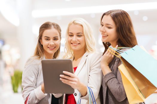 sale, consumerism, technology and people concept - happy young women with tablet pc and shopping bags in mall