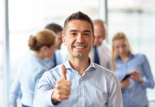 business, people, gesture and teamwork concept - smiling businessman showing thumbs up with group of businesspeople meeting in office