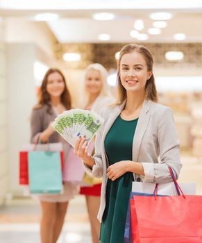 sale, consumerism and people concept - happy young women with shopping bags and euro cash money in mall