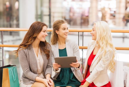 sale, consumerism, technology and people concept - happy young women with tablet pc and shopping bags in mall