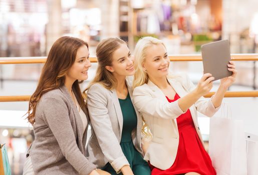 sale, consumerism, technology and people concept - happy young women with tablet pc and shopping bags in mall