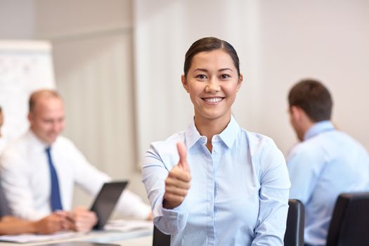 business, people, gesture and teamwork concept - smiling businesswoman showing thumbs up with group of businesspeople meeting in office