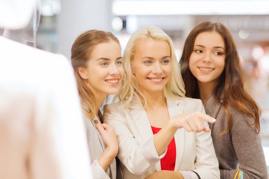 sale, consumerism and people concept - happy young women with shopping bags pointing finger to window in mall