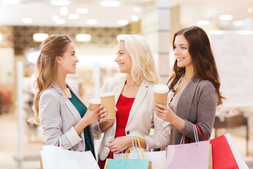 sale, consumerism and people concept - happy young women with shopping bags and coffee paper cup in mall