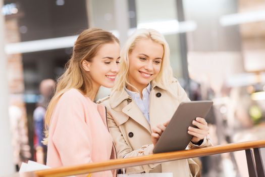 sale, consumerism, technology and people concept - happy young women with tablet pc and shopping bags in mall