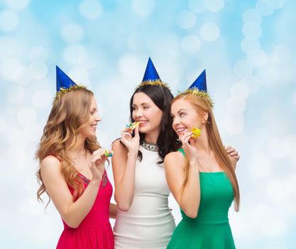 holidays, people and celebration concept - smiling women in party caps blowing to whistles over blue lights background