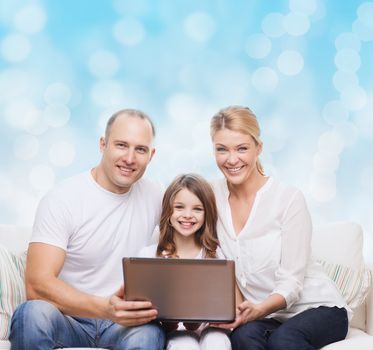 family, childhood, holidays, technology and people concept - smiling family with laptop computer over blue lights background