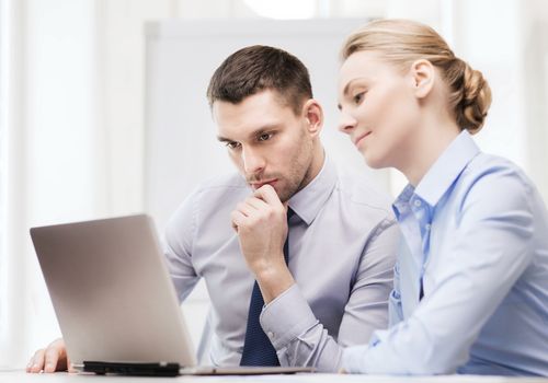 business, technology and office concept - serious businessman and businesswoman with laptop computer at office