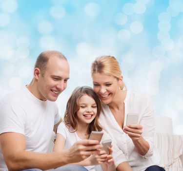 family, holidays, technology and people concept - smiling mother, father and little girl with smartphones over blue lights background