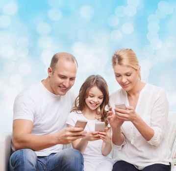 family, holidays, technology and people concept - smiling mother, father and little girl with smartphones over blue lights background