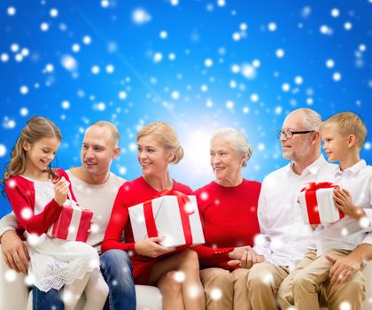 family, holidays, generation, christmas and people concept - smiling family with gift boxes sitting on couch over blue snowy background