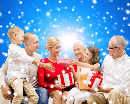 family, holidays, generation, christmas and people concept - smiling family with gift boxes sitting on couch over blue snowy background