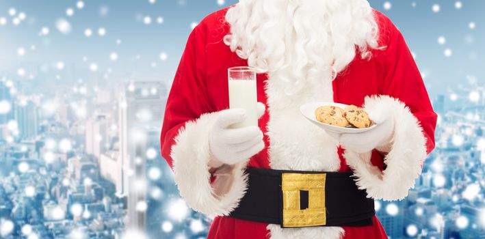 christmas, holidays, food, drink and people concept - close up of santa claus with glass of milk and cookies over snowy city background