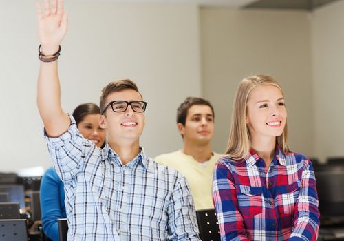 education, high school, teamwork and people concept - group of smiling students raising hand in lecture hall