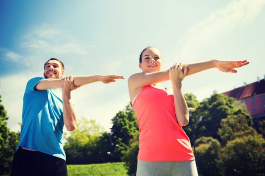 fitness, sport, training and lifestyle concept - smiling couple stretching outdoors