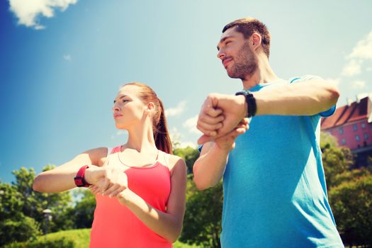 fitness, sport, training, technology and lifestyle concept - two smiling people with heart rate watches outdoors