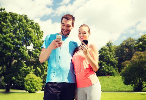 fitness, sport, training, technology and lifestyle concept - two smiling people with smartphones and earphones outdoors