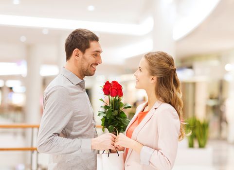 relations, love, romance and people concept - happy young couple with flowers talking in mall