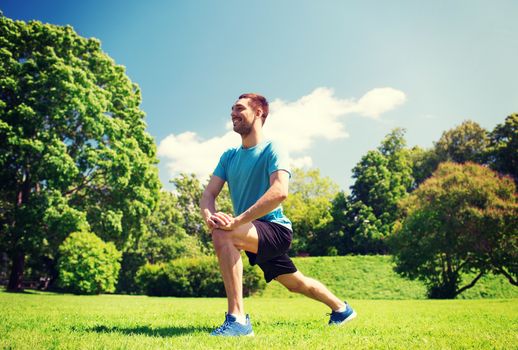 fitness, sport, training and lifestyle concept - smiling man stretching leg outdoors