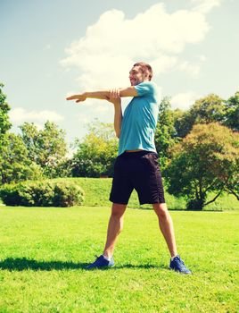 fitness, sport, training and lifestyle concept - smiling man stretching hand outdoors