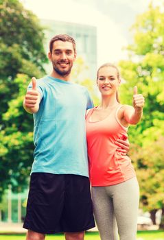 fitness, sport, friendship and lifestyle concept - smiling couple outdoors showing thumbs up