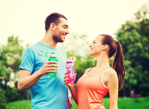 fitness, sport, friendship and lifestyle concept - smiling couple with bottles of water outdoors