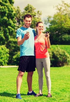 fitness, sport, training, technology and lifestyle concept - two smiling people with smartphones and earphones outdoors