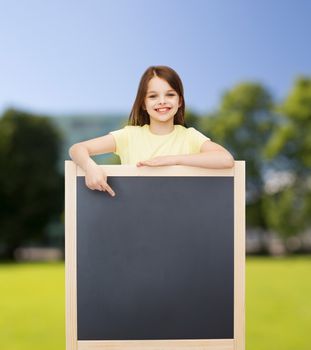 people, advertisement and education concept - happy little girl pointing finger to blackboard