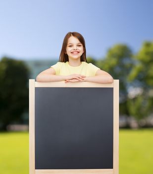 people, advertisement and education concept - happy little girl with blank blackboard